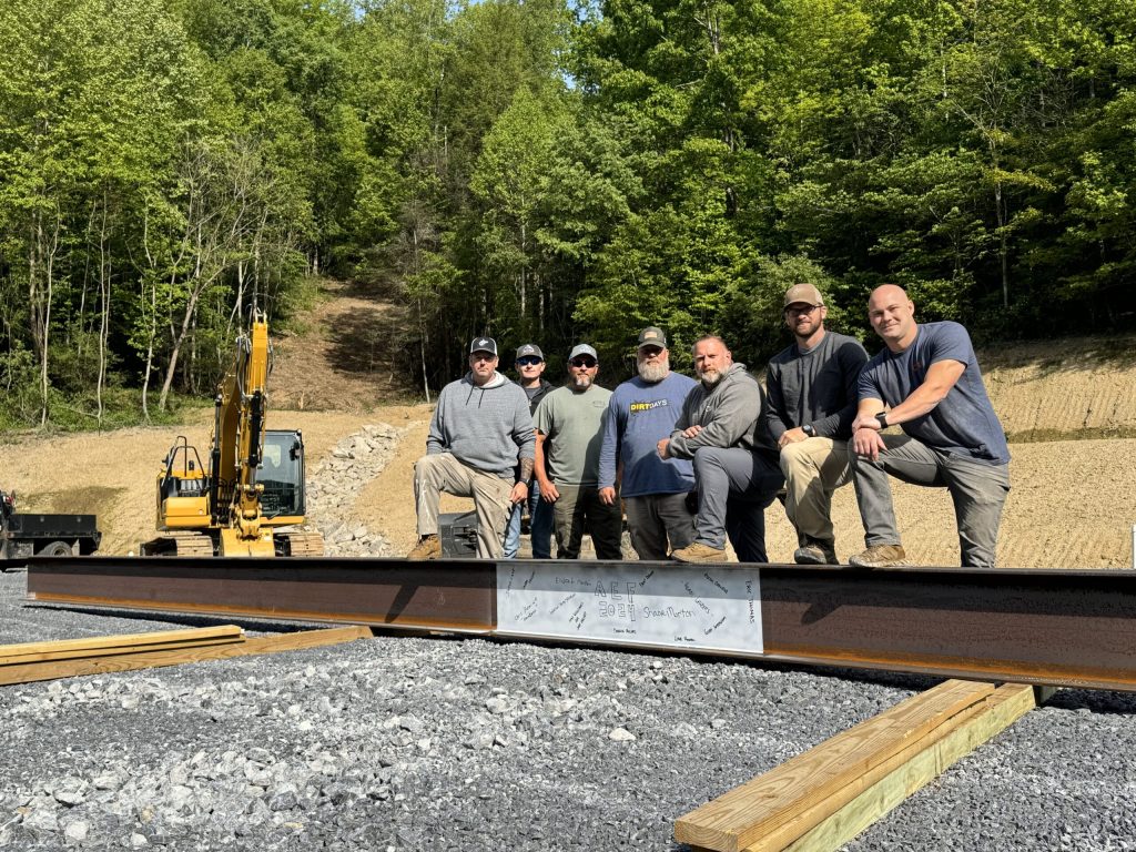 People stand next to a large steel beam with signatures on it.